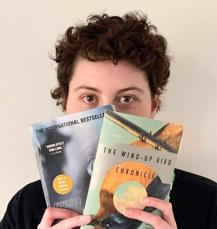 Mouse Larisheva, an adult white man with curly hair, holds two books in front of the bottom half of his face.